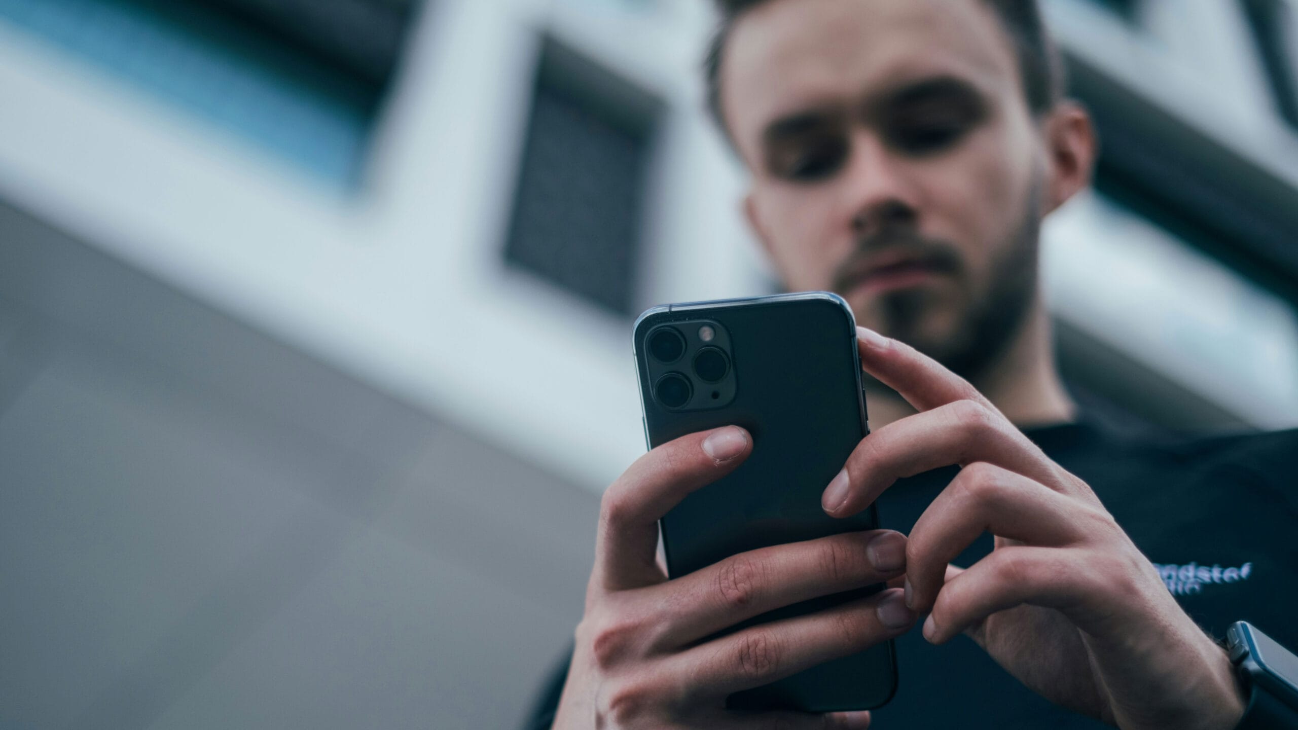 Eine Person schaut auf ihr Smartphone, Perspektive von unten aufgenommen, im Hintergrund sieht man verschwommen eine Hausfassade.
