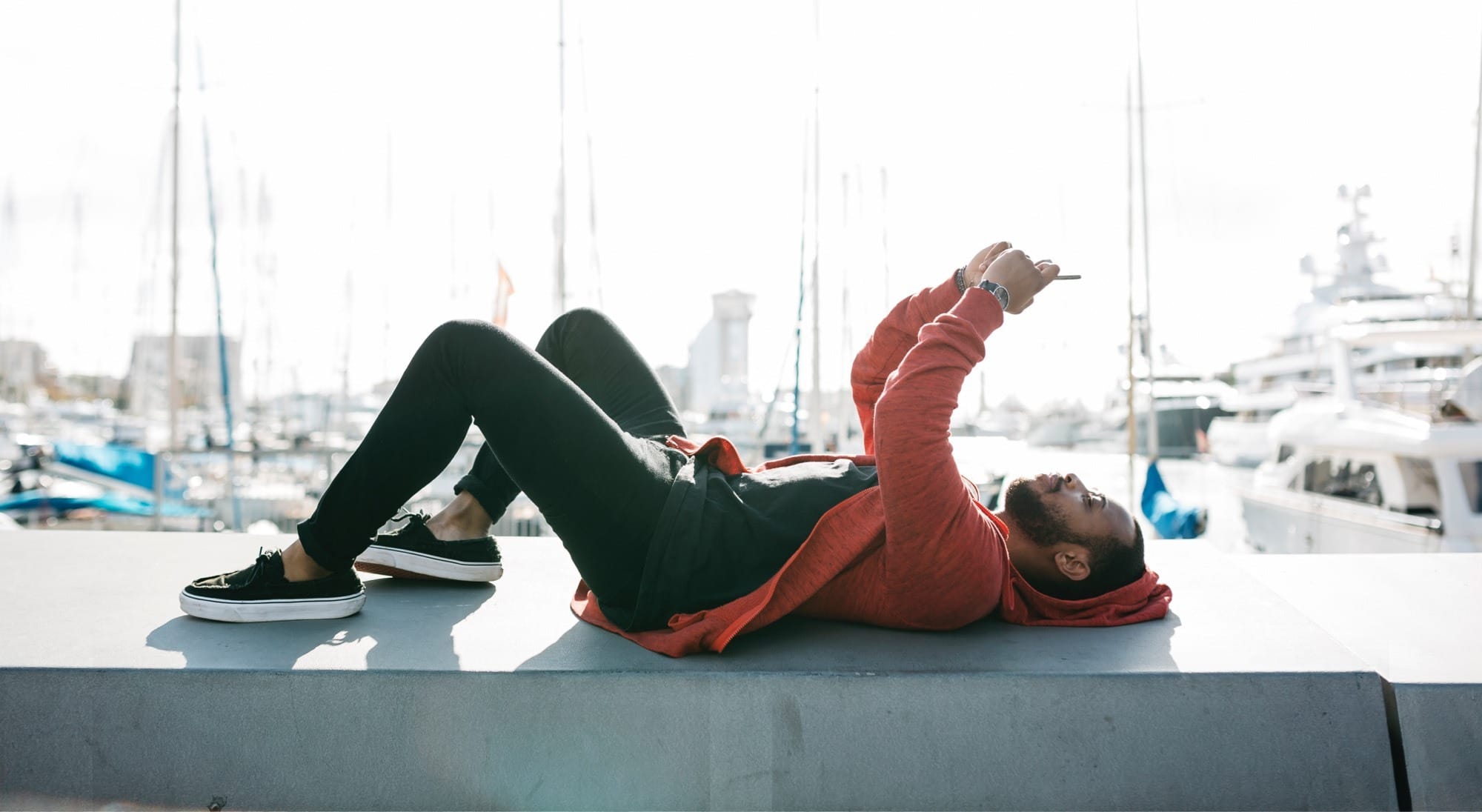 cyan Keyvisual – Mann benutzt Smartphone am Rücken liegend in der Freizeit im Yachthafen