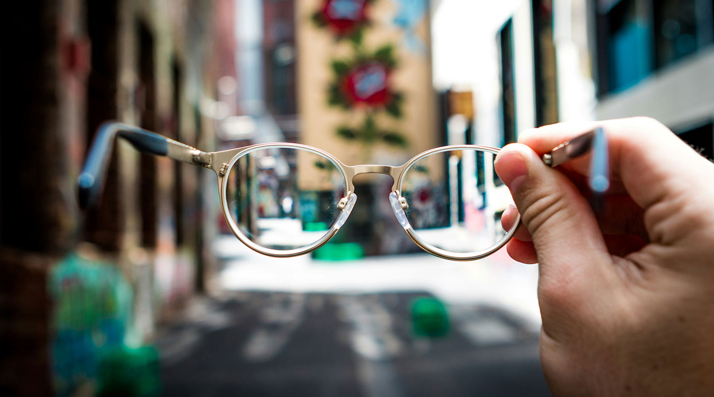 Eine abgenomme Brille in der Hand vor einer Straßenszenerie im Hintergrund - Symbolbild zu Barrierefreiheit einer Website testen