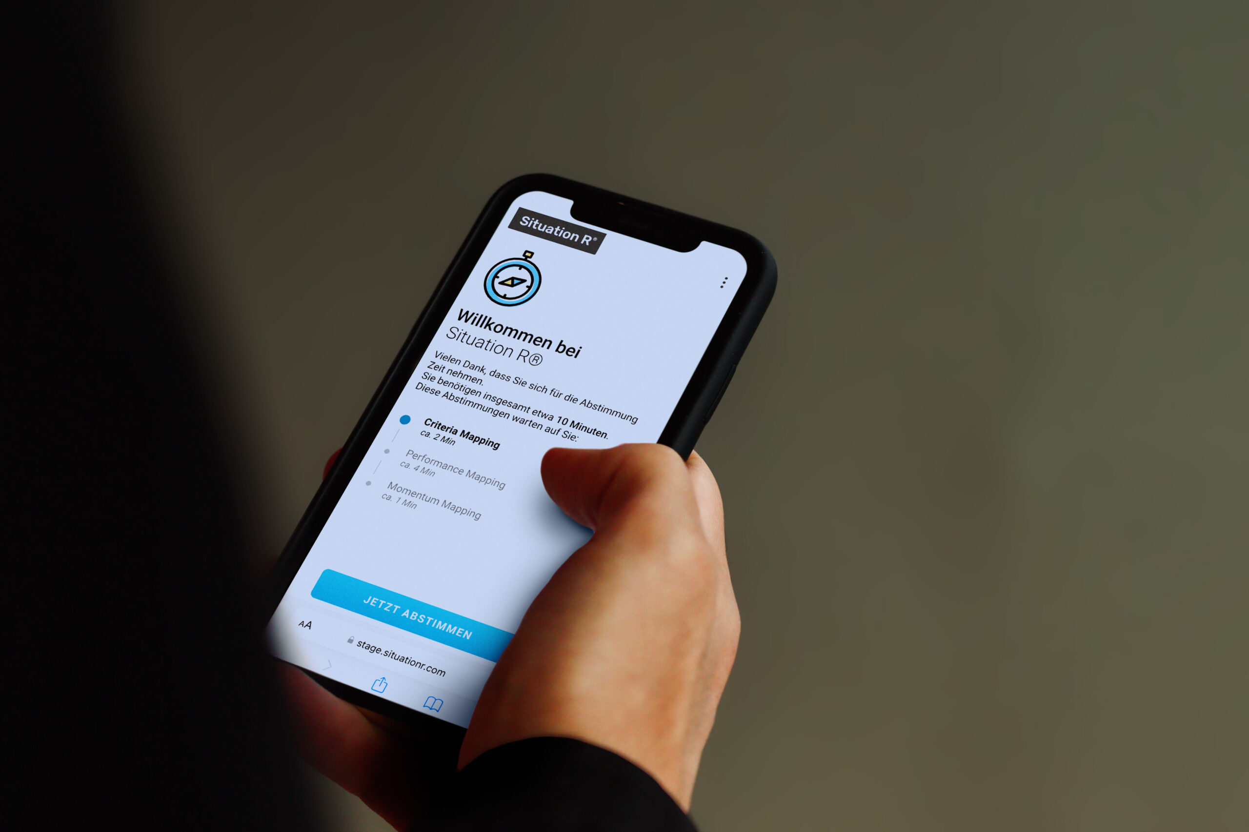 Eine Hand hält ein Smartphone auf dem der Wilkommensscreen von Situation R zu sehen ist - Workshop-Software mit KI Integration